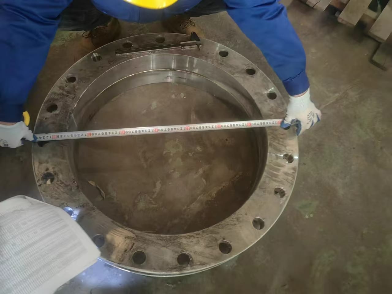 Measuring a fabricated steel flange against the drawing with a tape measure, on-site in Jiangsu